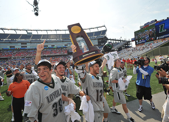 Graduate student and attackman Eric Lusby holds the NCAA National Championship trophy up, surrounded by his teammates.