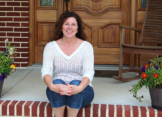 Beth sits on a brick step in front of her home, smiling.