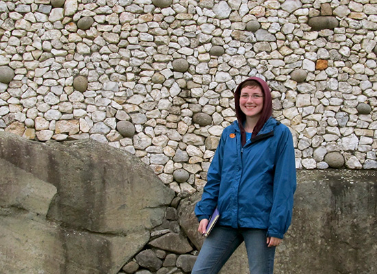 Rory in front of an old, stone wall, smiles at the camera.