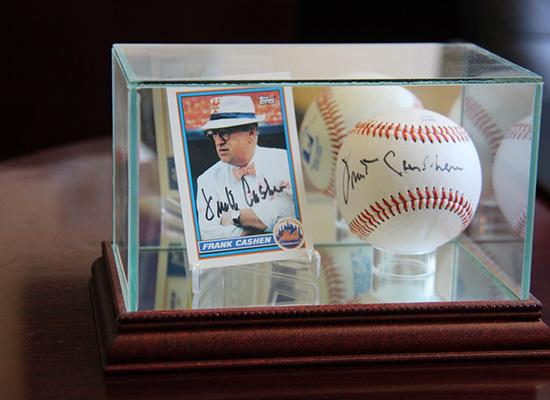 Card and signed baseball of Frank Cashen in a glass display box.