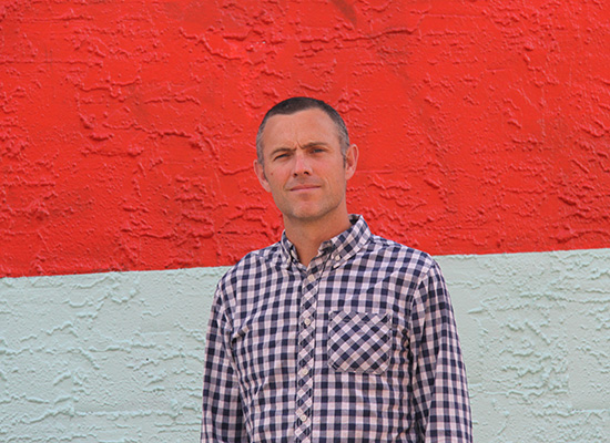 Photo of Tom Butler in front of a red and white, duo color wall.