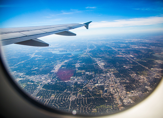 Plane window overlooking aircraft wing, blue horizon, and the earth below.