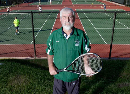 Rick McClure holding a tennis racket in front of tennis courts