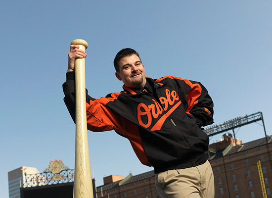 Steve Butz leaning on large baseball bat and wearing his Orioles jacket.