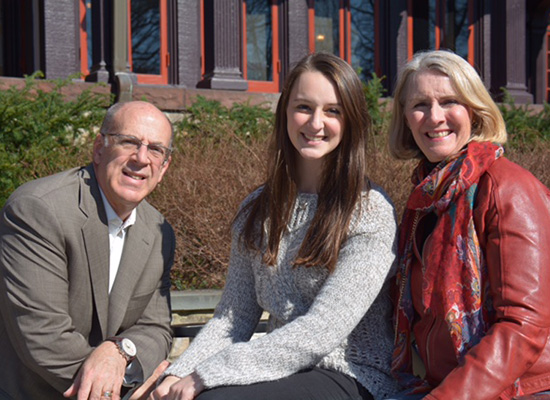 Meredith sitting with her parents in front of the humanities manor.