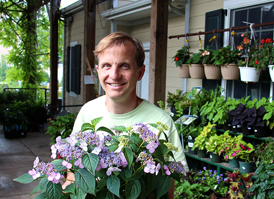 Peter Bieneman surrounded by pots of various plants and flowers.