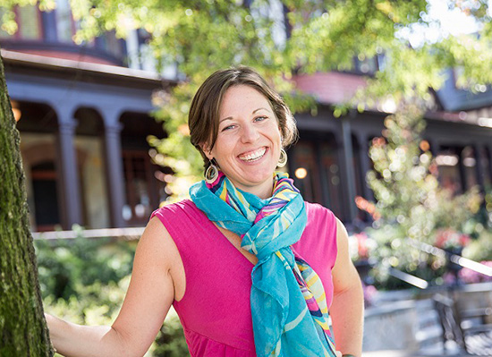 Erin smiling and standing by a tree in front of humanities manor.