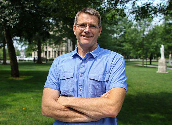 David Carey, Jr., Ph.D. crossing his arms under the sun in Loyola's quad.