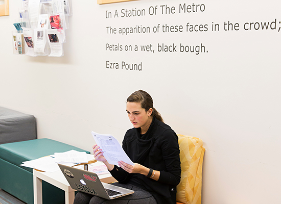 Student sits and reads paper in the writing department hallway.