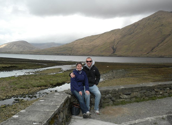 Dan and Lindsay sitting on a stone barrier with mountains behind them.