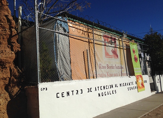 Wall beneath barbed wire bears letters and old signs.