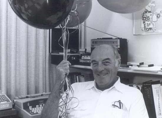 Charles Hands sitting in a chair holding a bundle of helium balloons.