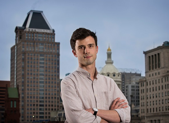 Photo of Patrick Diamond crossing his arms with Baltimore's skyline in the background.