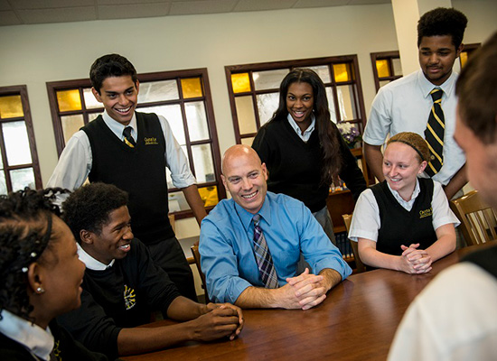 Bill Heiser sits at a desk, surrounded by students.