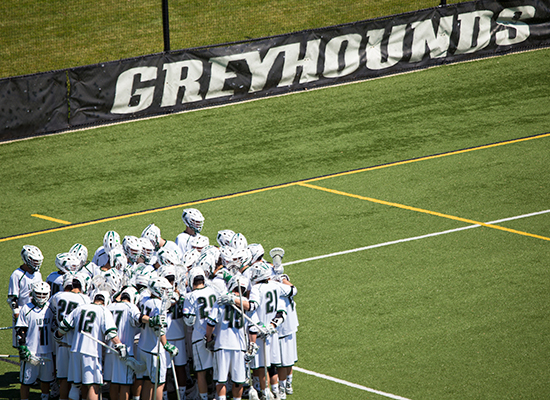 Greyhounds lacrosse team huddles together on the field.