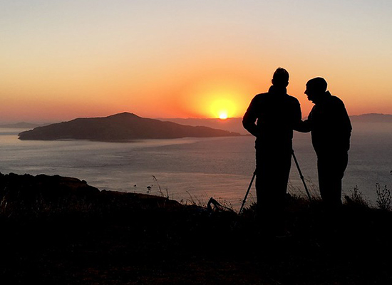 Silhouettes of an elderly and middle aged man, overlooking the sunset across the sea.