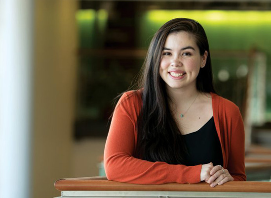 Female student leans on railing, smiling at the camera.