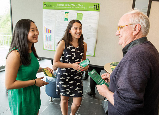 Two students with professor stand in front of presentation.