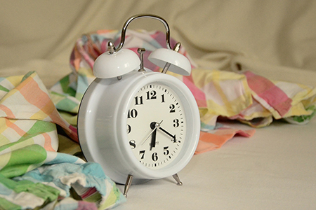 Small, white clock surrounded by pastel and white fabrics.