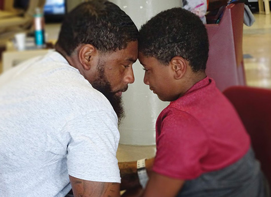 Father and son sit together, forehead to forehead.