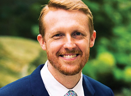 Jim Dickinson smiles, wearing a blue suit in outdoor portrait.