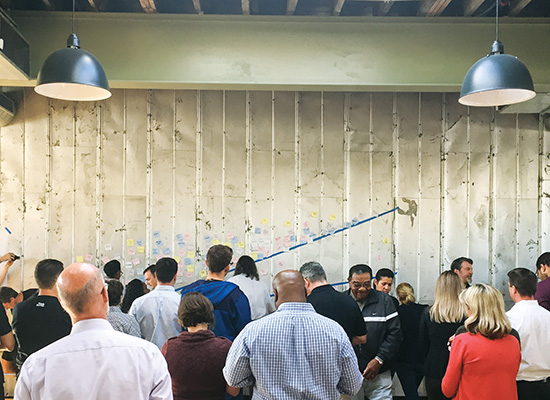 Crowd gathers around interactive wall display of sticky notes.