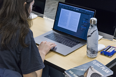 Apprentice House female student reads a manuscript on her laptop.