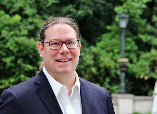 Allen Brizee smiles for a photo, with trees blurred in the background