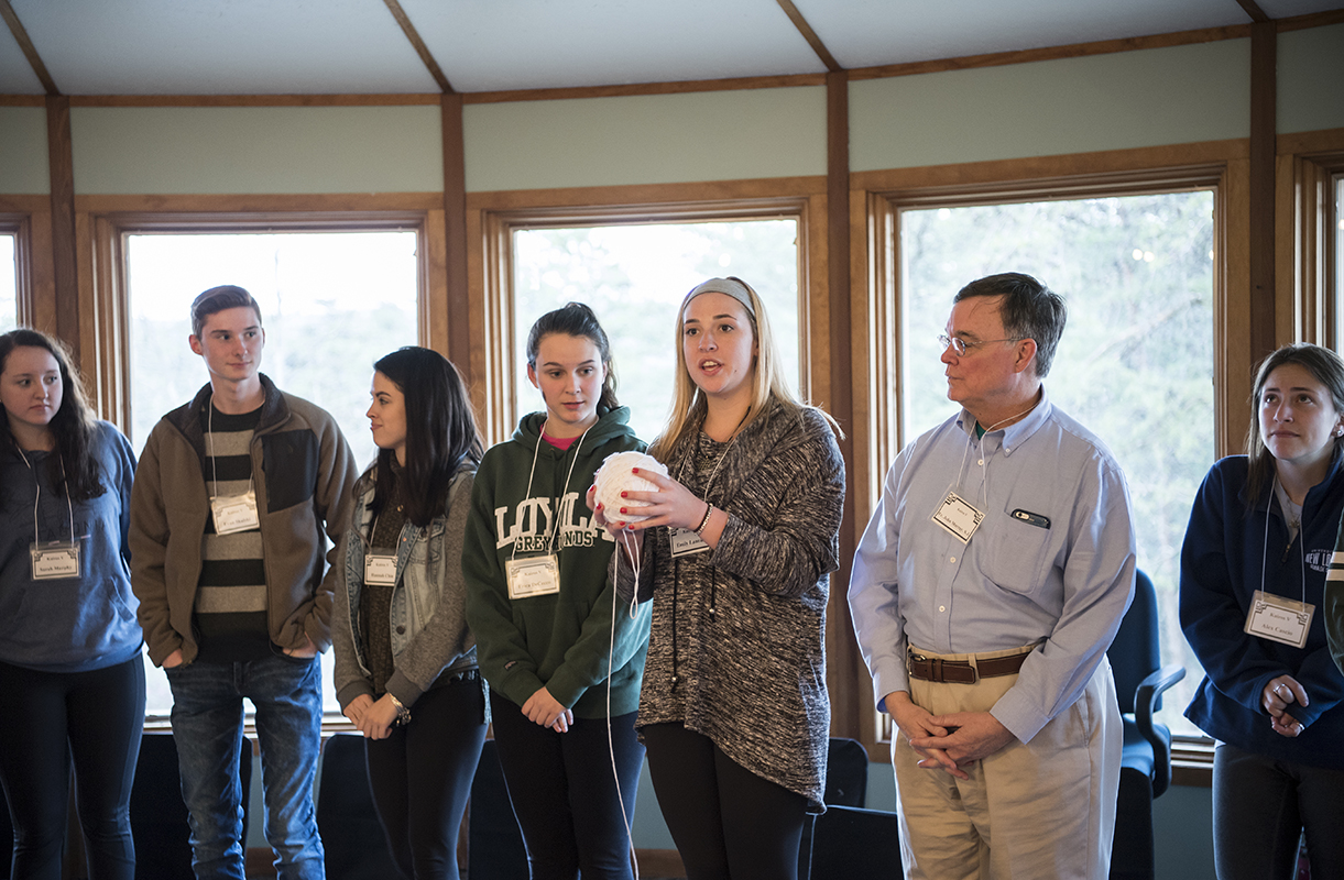 Students wear name tags and stand in a circle as a retreat leader explains an activity.