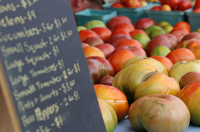 A chalkboard with produce prices next to tomatoes of various colors