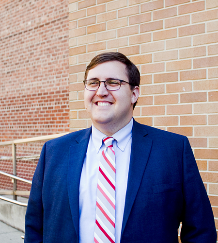 John Dougherty smiling in front of brick wall background.