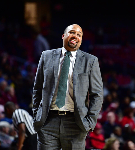 Hardy in a grey suit smiling on the court during a game.