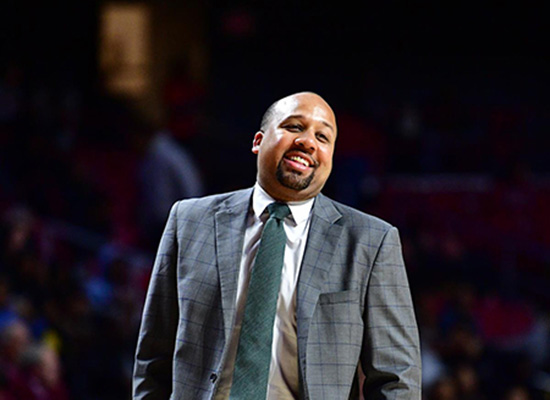 Hardy in a grey suit smiling on the court during a game.