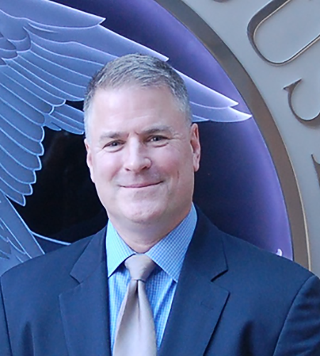 Kevin Dowling smiles in portrait, wearing a blue suit.