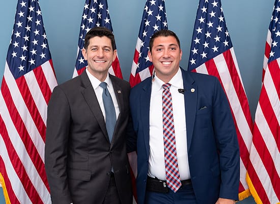 Zach Samson and Paul Ryan standing in front of American flags