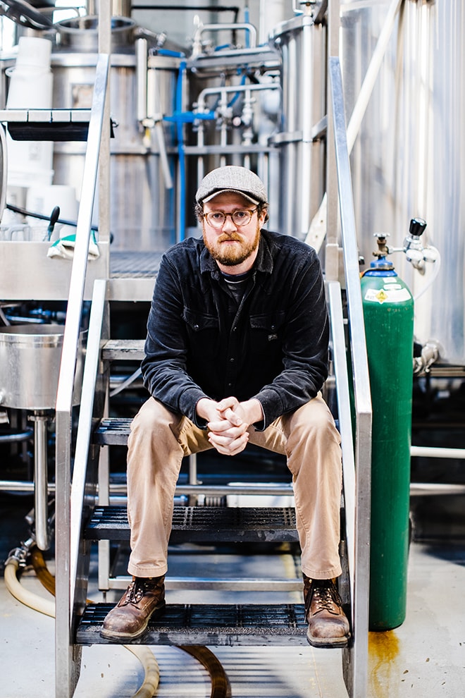 Ryan Fitzpatrick posing for a photograph sitting on the steps of the inside of his brewery