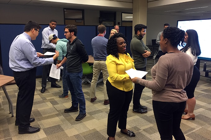 Students stand in pairs rehearsing for a pitch competition