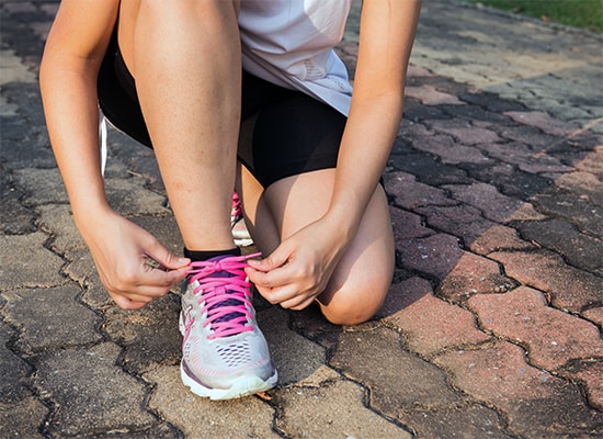 Photo of a person in running clothes kneeling down to tie their shoes