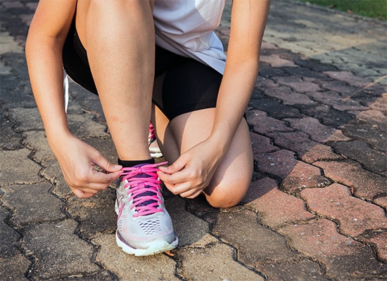 Photo of a person in running clothes kneeling down to tie their shoes