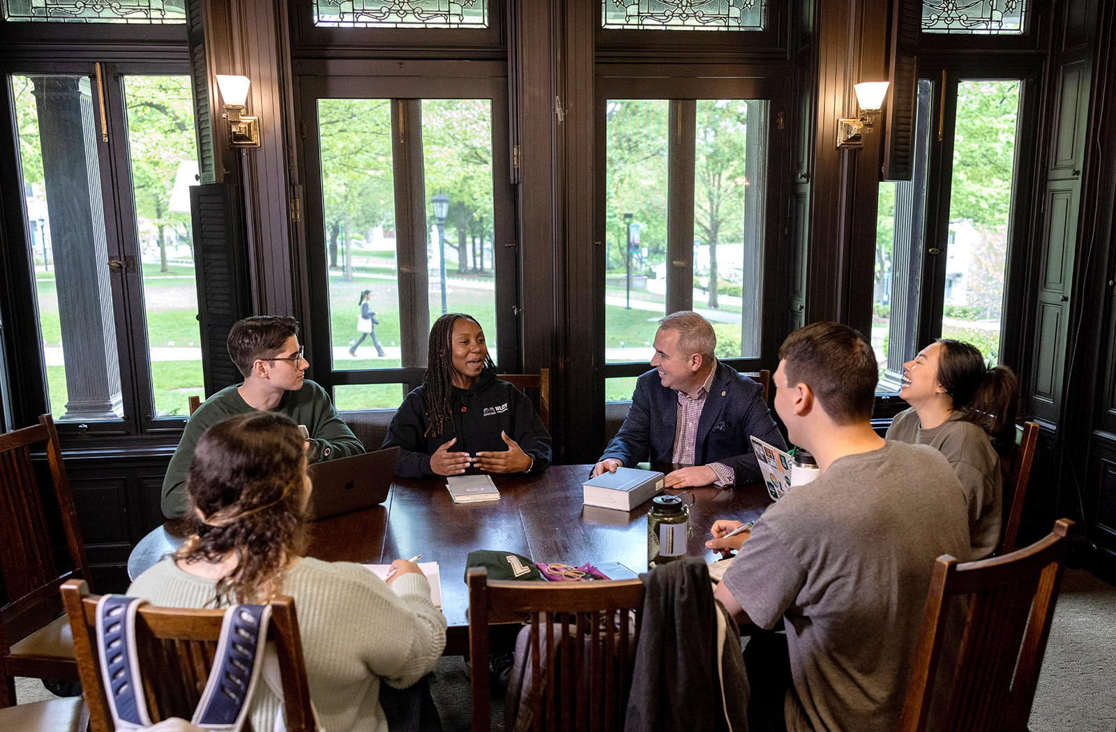 President Terry Sawyer and a group of students sitting around a table talking and laughing