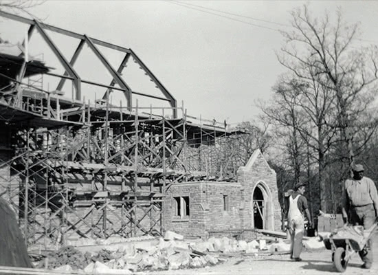 Black and white photo of two workers pushing wheelbarrows and surveying the site of a Alumni Memorial Chapel during its construction