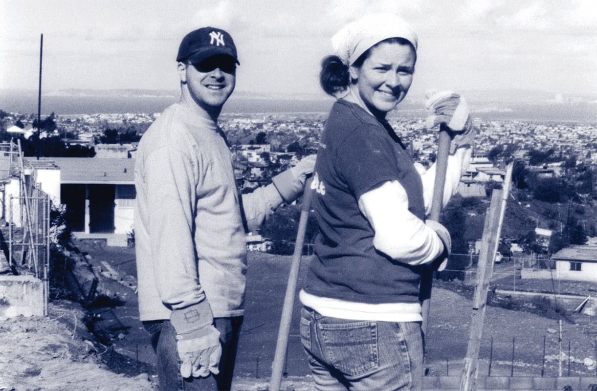 Black and white photo of two students posing for a photo in Mexico while holding gardening equipment