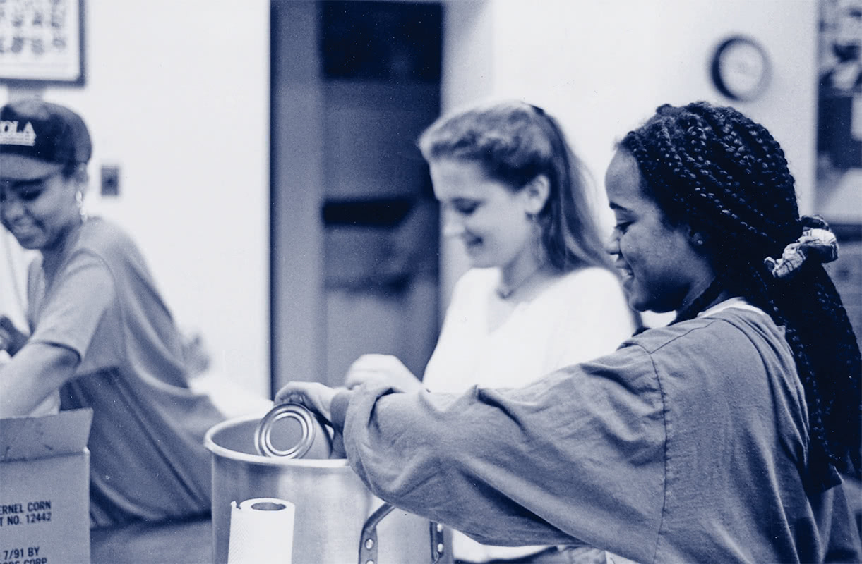 Black and white photo of students smiling while volunteering at a food pantry