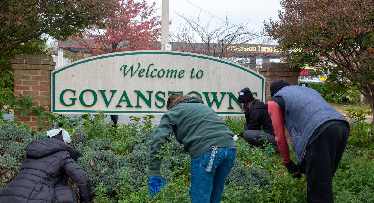 Students clearing out weeds in front of a Govanstowne sign