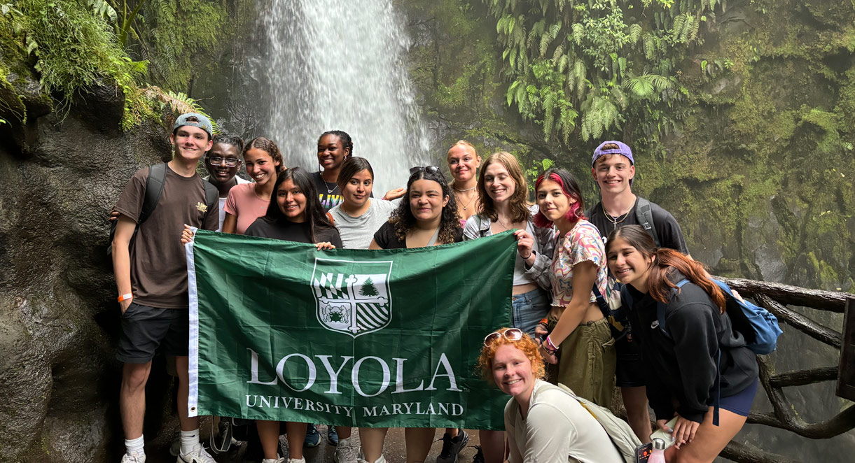 Students in front of a waterfall holding a Loyola flag