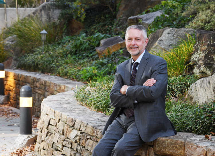 Chis Miller smiling for the camera while sitting on a rock retaining wall