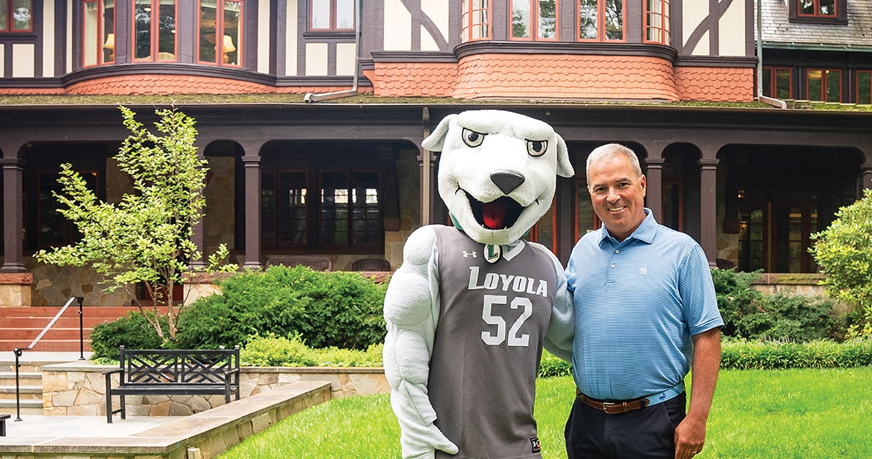 President Terry Sawyer standing outside of the Humanities Buildling with Iggy, the Loyola Mascot