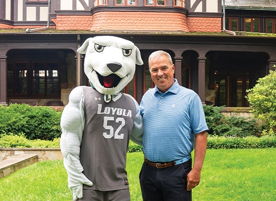 President Terry Sawyer standing outside of the Humanities Buildling with Iggy, the Loyola Mascot