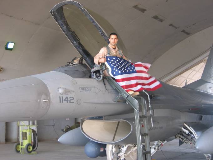 Ernie Bio holding an american flag seated in the cockpit of a jet plane