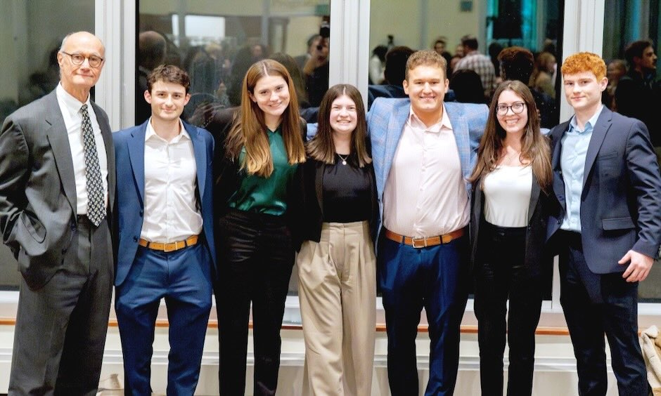 A group of 6 students and their professors in business attire.